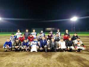 ライトがで照らされた夜の野球グラウンドの上で、市長を中心に参加者たちが3列になり写っている記念写真