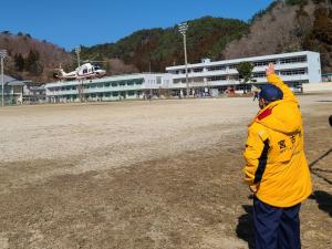 訓練会場に下りてくるヘリコプターに向かって、市長が手を挙げている写真
