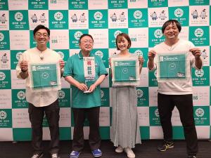 バックパネルの前で小さな旗を手にする市長とハンカチのようなものを広げる天津木村さん、アンダーエイジのたもんさん、タレントの吉田有希さんが写った記念写真
