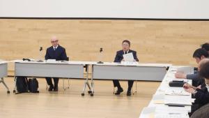 広い会議室内で、マイクが置かれた長机の席につく山本市長の写真