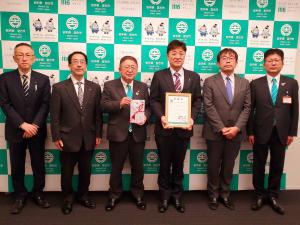 市長が寄贈いただいた目録持ち、参加された郵便局長会の1名が市からの感謝状を持ち、関係者を含めて6人で並んで撮影した写真