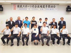 「国民スポーツ大会出場選手激励会」と書かれた横断幕が貼られた部屋で、選手と関係者の方々と市長が右手でガッツポーズをして撮影した写真