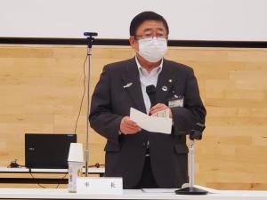 市長が自席で立ち、資料を広げてマイクを持って話をしている写真