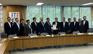 木目調の長机が設置された会議室内で、中央に自由民主党の梶山弘志幹事長代行と市長会の代表が一緒に要望書を持って中央に立ち、市長を含む11名の関係者が横一列に並んでいる写真