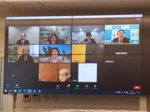 天井から吊るされたスクリーンに、ウェブ会議の参加者たちの画面が分割して映されている様子の写真
