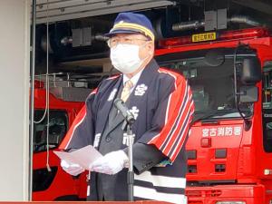 消防車の前で、法被を着て制帽を被った市長が資料を持ちスタンドマイクの前で話をしている様子の写真
