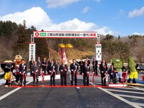 多くの参加者が見ている中、開通した道路上のレッドカーペットで市長の他7人で紅白のテープカットをおこなった写真