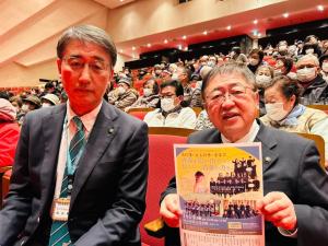 「高校生による新春の音楽祭」のチラシ見せながら市長と関係者の男性1名が市民文化会館で鑑賞をしている様子を写した写真