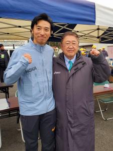 青と白のストライプ柄のテントの前で、市長とランニングトレーナー鳥光健仁さんが並んでガッツポーズをしている記念写真