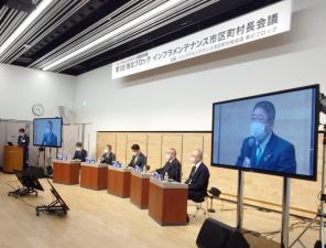 東北ブロックインフラメンテナンス市区町村長会議と書かれた横断幕の下に出席者5人がそれぞれの席に座り、市長がモニターに映し出された写真