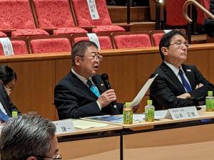 シンポジウムの会場の席で右手にマイクを持ち話をしている市長の写真