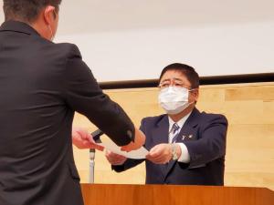 檀上に立つ市長が、男性の職員に辞令を手渡している辞令交付式の様子の写真