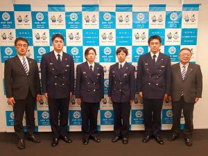 制服を着た消防職員の男女4名を中心に、両側に男性1名と市長が立ちバックパネルの前で並んでいる写真