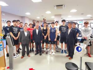 運動器具などが置かれた施設の中で、3列に並ぶ市長、関係者2名と学生たちを写した写真