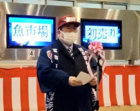魚市場、初売りとそれぞれ表示されるモニターの前で、市長が帽子を被り、法被を着て、式辞を述べている写真