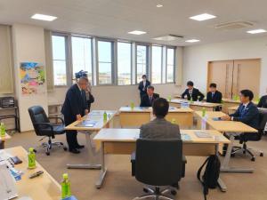 会議室で4人の首長が向かい合う形で席につき、山本市長が立って話をしている様子の写真