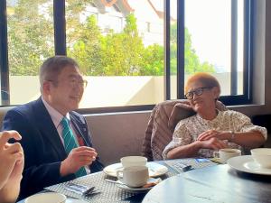 コーヒーカップが置かれた円卓の席に着き話をする様子の市長とフィリンピンのラ・トリニダッド市タバンダ前市長の写真