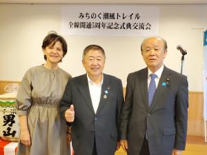「みちのく潮風トレイル全線開通5周年記念式典交流会」と書かれた紙が貼られた壁の前で、市長を中心に八木環境副大臣、ヨルダン王国のリーナ大使が横並びに立つ記念写真