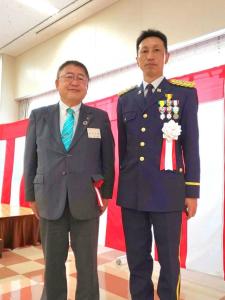 紅白幕の前で横に並ぶ市長と胸章を付け、勲章を付けた制服姿の自衛官が写った記念写真