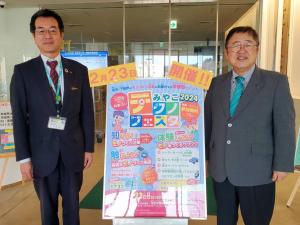 「みやこ2024テクノフェスタ」のポスターをはさんで市長と関係者の男性2名で記念撮影をしている写真
