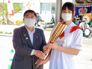 スーツ姿の市長が聖火ランナーのユニフォームを着た女性と聖火リレーで使用するトーチを持っている写真