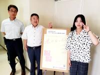 立て看板の横に立つ市長と山岸聖恋(せれん)さんと関係者が並んでいる写真