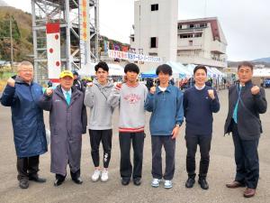 マラソン大会の会場で、市長を中央に中央大学陸上競技部の4名の選手と2名の関係者が横一列に並びガッツポーズをしている記念写真