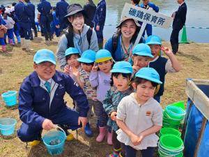 市長と磯鶏保育所のプラカードを持った2名の保育士と青い帽子を被った7人の園児たちが笑顔で写っている集合写真