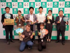 バックパネルの前で団扇を持った市長とお茶のケースを持った副市長の間に男性2名、女性4名が集合して、それぞれ団扇やペットボトルのお茶を持っている写真
