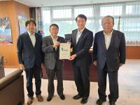 壁に大きなポスターが貼られた室内で、国土交通省の泉田裕彦大臣政務官と市長が要望書を一緒に持ち、宮古市議会の橋本久夫議長と宮古商工会議所の大坂文人副会頭が横一列に並んでいる写真