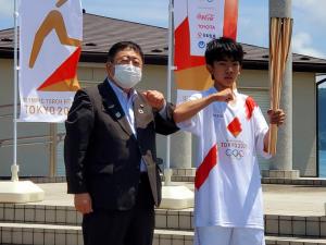 スーツ姿の市長が聖火ランナーのユニフォームを着て、左手で聖火リレートーチを持っている男性と肘タッチをしている写真
