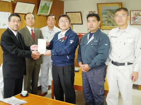 応接室で、市長とスーツや作業着姿の男性5名がおり、スーツ姿の男性が、市長に寄付金を手渡す写真