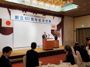 ステージに「東北ヒロセ電機株式会社創立50周年記念式典」と書かれた幕の前の演台で挨拶をしている市長の写真