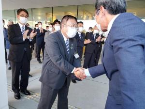 握手をする市長と佐藤廣昭副市長、後方で拍手をして2人を見ている様子の大勢の職員の方々を写した写真
