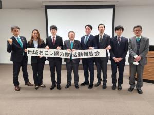 中央に市長、左端に副市長、その間に隊員6名が立ち、地域おこし協力隊活動報告会と書かれた紙を持って並んで撮影した写真
