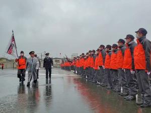 雨が降る中1列に並んでいる消防団員の前を市長と関係者の方が歩いている出初式での写真