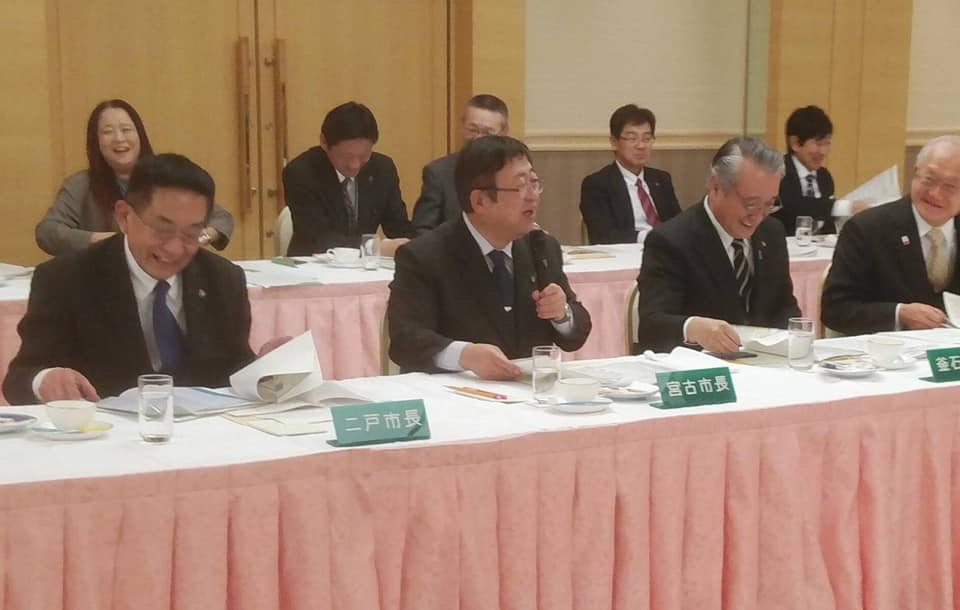 前列に岩手県内の市長の方々、後列に関係者の方々が座っている会場で、左手にマイクを持った市長の話を聞いている周囲の市長や関係者の方々が笑顔になっている会議の様子の写真