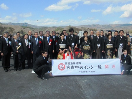 新しい道路の上で、「宮古中央インター線 開通」の横断幕を手に持ち、市長や関係者が集合し、並んでいる写真