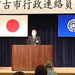 2枚の旗と横断幕が掲げられたステージ上の檀上で、マスクをつけた市長が話をしている写真