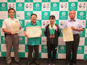 全国高校インターハイ卓球選手権大会で、女子ダブルス準優勝を果たした小林りんごさんがバックパネルの前で首からメダルを二つかけ両腕を後ろで組み笑顔を浮かべ、小林りんごさんの隣に賞状を持った市長、両端にも賞状を持った2名の関係者の男性が横一列に並んでいる記念写真