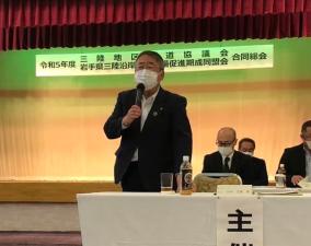 白いテーブルクロスが引かれた机の上後ろに立ち、右手にマイクを持って発言しているスーツを着た市長の写真