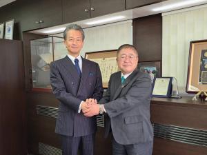 賞状が並べられた応接室のような部屋で、市長と男性が握手している写真