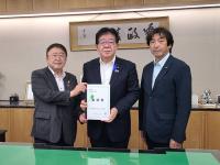 書が飾られた室内で、総務省の金子恭之大臣と市長が要望書を一緒に持ち、宮古市議会の橋本久夫議長と横一列に並んでいる写真