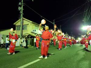 赤い着物を着て頭にハチマキを巻き右手に持った団扇を上に掲げながら踊る様子の市長と、その周りで列を作って踊る参加者の写真