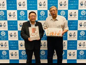 バックパネルの前でトラウトサーモン詰め合わせの箱をもつ市長と男性の写真
