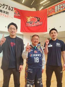 ユニフォームを着た市長とその両サイドに立つ男性2人が右手の人差し指を上に向けポーズを決めて写真撮影をしている写真