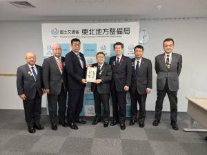 「国土交通省 東北地方整備局」と書かれたバックパネルの前で、要望書を一緒に持つ男性と市長を中心に、左側に男性が2名、右側に男性が3名横並びになって写っている写真
