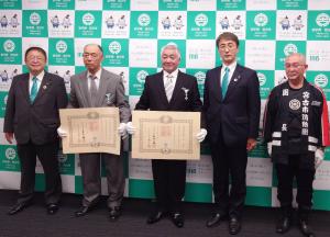 宮古市のバックパネルの前で瑞宝単光章を受章された佐々木榮一郎さん、藤岡豊さんが感謝状を両手で持ち、その両サイドに市長と関係者が並び記念撮影している写真