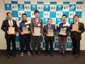 市長と他の職員の方、丸光商事の方々の計6人が寄贈いただいた童話を持ち、並んで撮影した写真