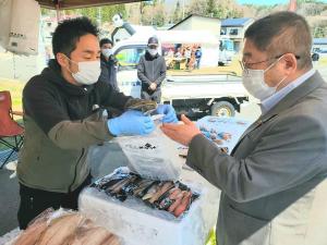鍬ヶ崎元気市に出店した海産物を販売しているお店で、スタッフの男性から商品を購入している市長の写真